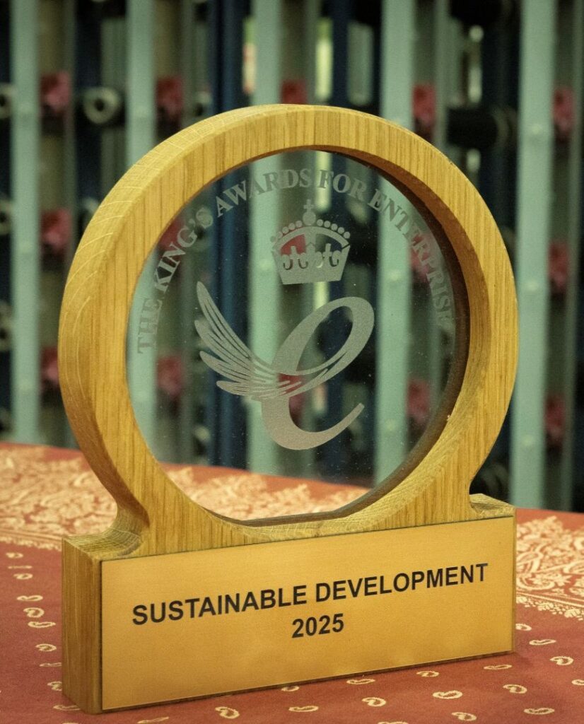 Wood and glass award on table, engraved with King's award logo, with cones of yarn in the background