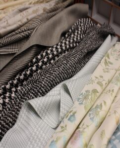 SS27 Apparel Fabrics laid next to each other including a pastel floral, a brown plain and a monochrome check.