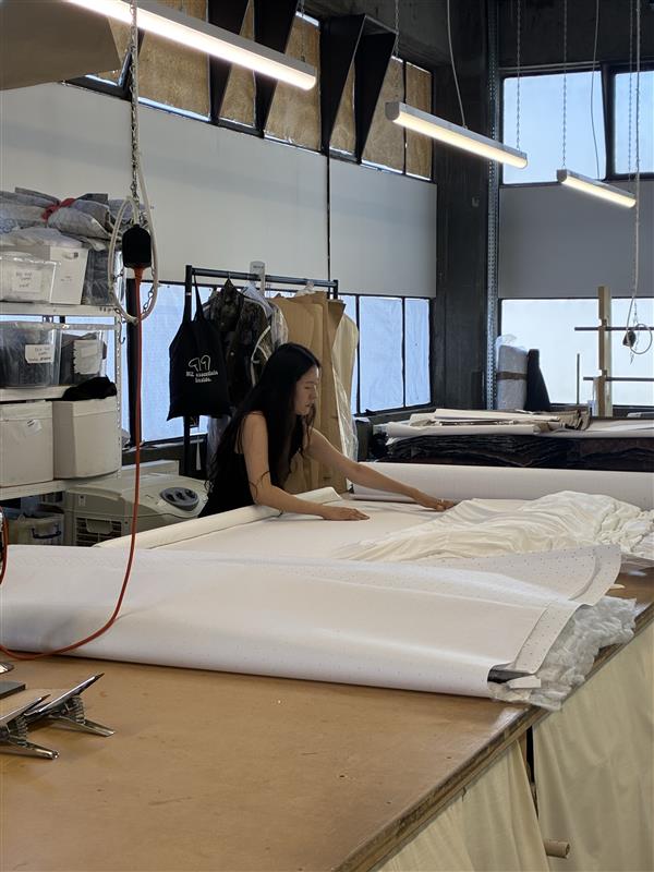 A lady cutting some white fabric for garments from a lay plan at Maes London