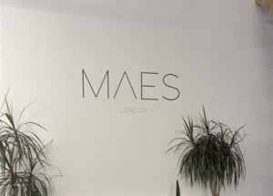 Maes London luxury manufacturer sign on wall with green houseplants underneath.