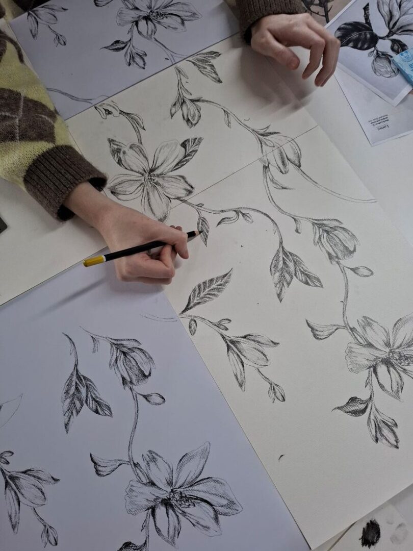 Hands sketching a bespoke development some black and white flowers with pencil on white paper.