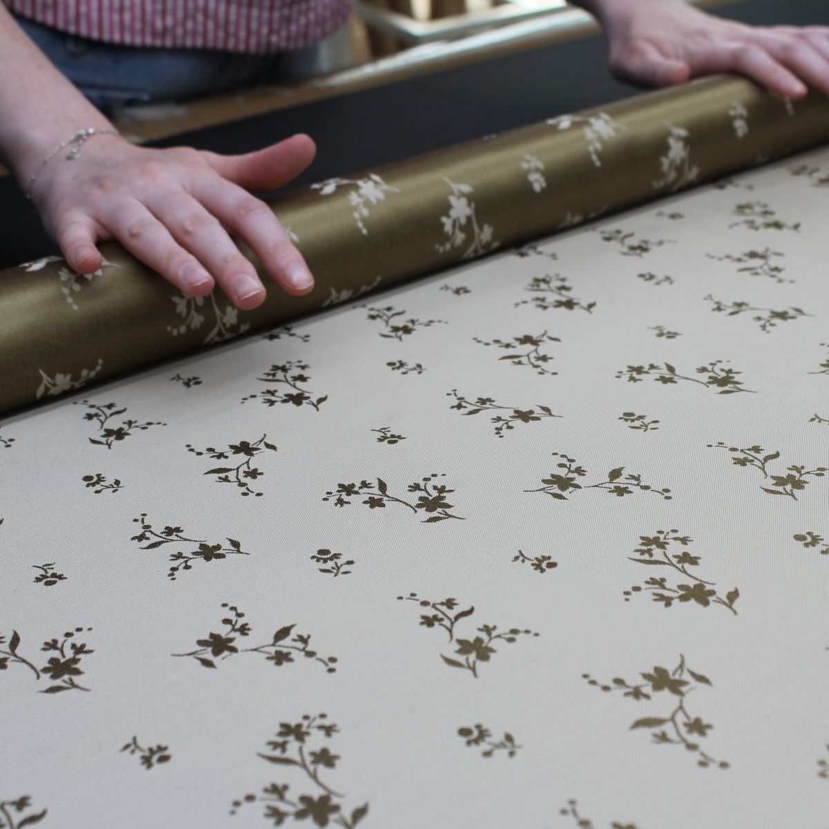 A woven Stephen Walters white fabric with a gold flower fabric being rolled onto a tube on an inspection table.