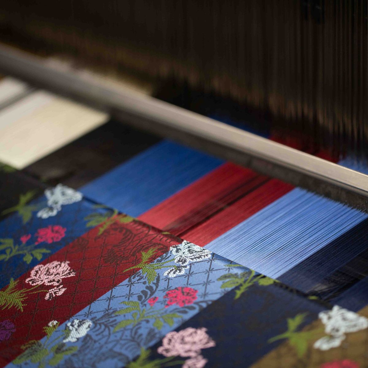 A close up of an ornate pink and white floral Stephen Walters apparel design on a weaving loom across a multi coloured weaving warp.