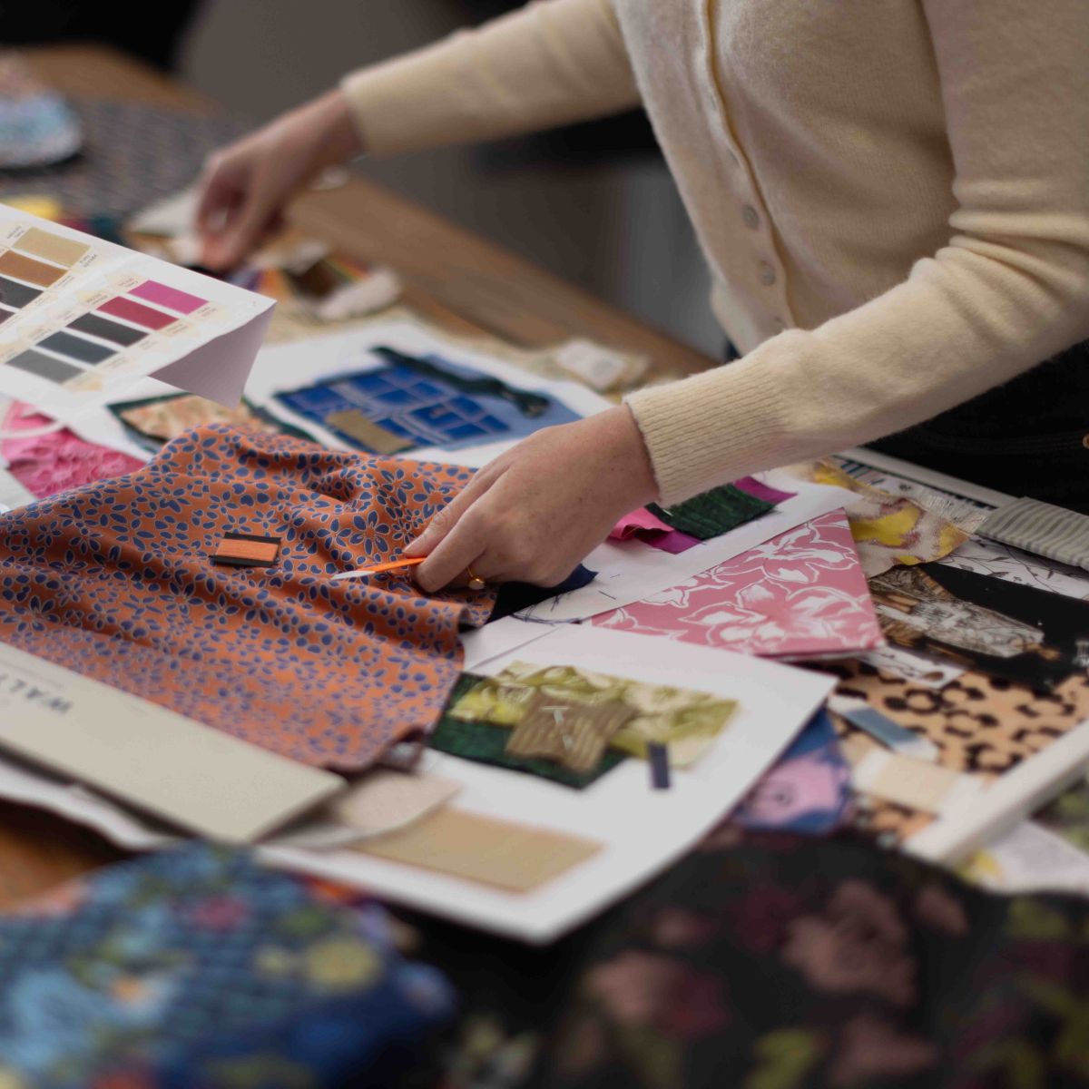 Multiple fabrics scattered on the Stephen Walters showroom table in an array of colours with a customer holding some of the fabrics.